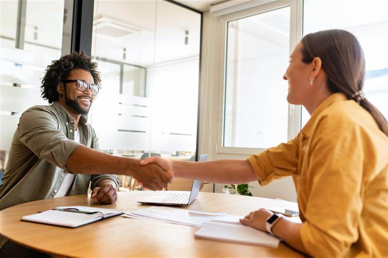 Two people sat at a table, shaking hands.