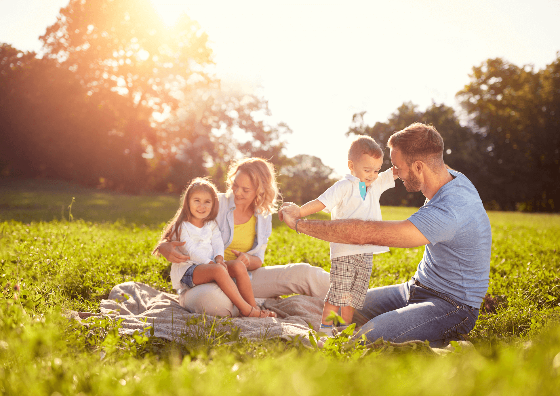 parents with two young children playing outdoors on a picnic blanket