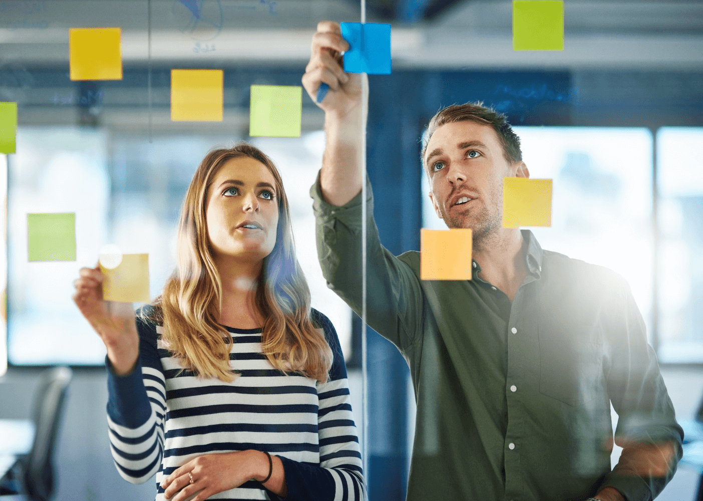 Male and female employees casually dressed, sticking post-it notes on a glass board