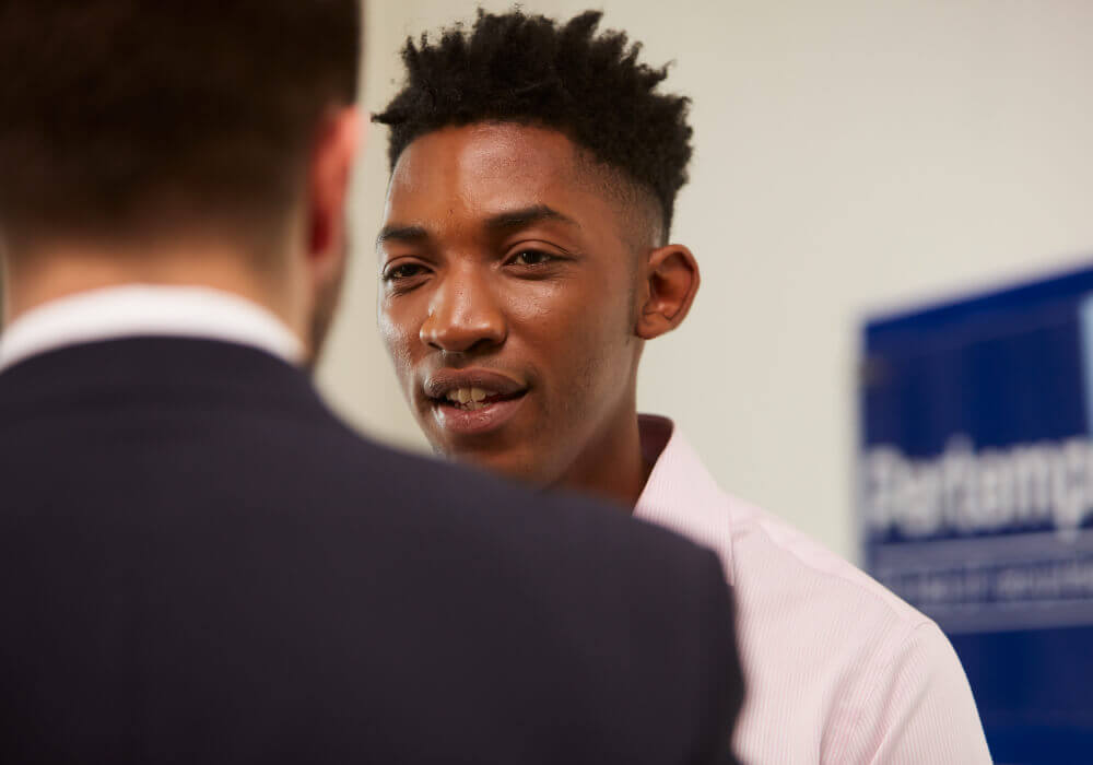 Two smartly dressed men having a conversation by a Pertemps sign