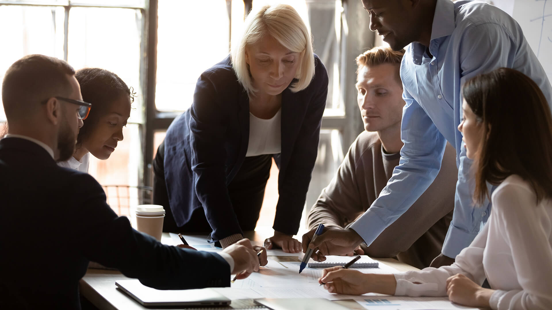 Concentrated middle aged female team leader leaning over table