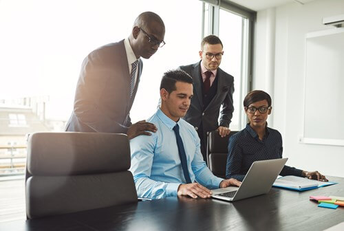 Smartly dressed employees gathering around a laptop